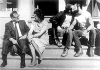Man and woman sit on steps near two kissing men